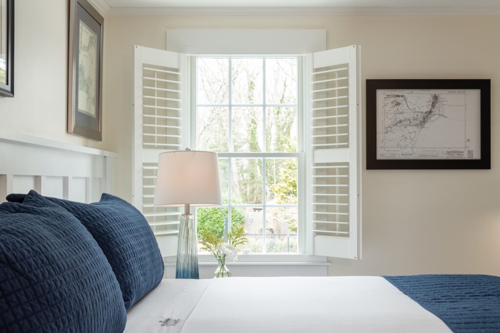 A bed by a window with art on the walls at a Bed and Breakfast in Cape Cod.