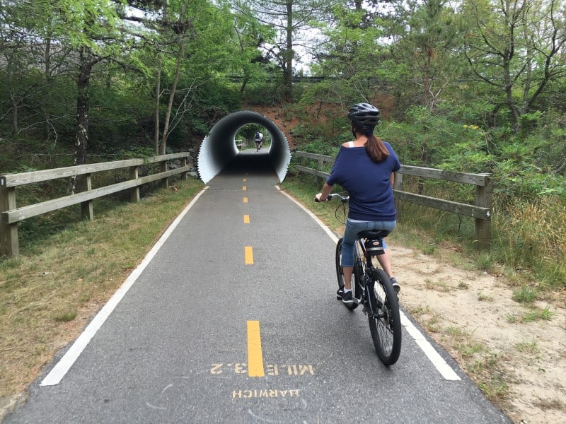 What to do on Cape cod in the Spring 1 A woman in a blue shirt and jeans wearing a helmet riding a bicycle on the Cape Cod Rail Trail