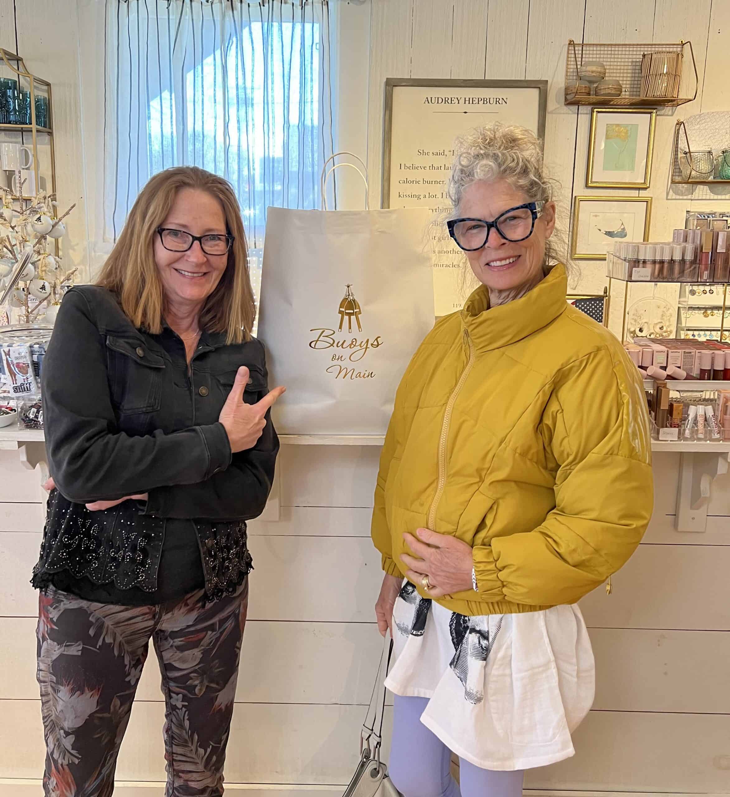 What to do on Cape cod in the Spring 2 Two women in a store. One is blond with red eye glasses and wearing a yellow puffy coat. The other is wearing black eye glasses, a black bejeweled jacket and is pointing at a white shopping bag.