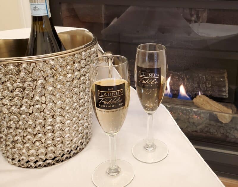 Two champagne glasses on a table in front of a fireplace with a crystal champagne bucket off to the side - at the best Cape Cod Bed and Breakfast