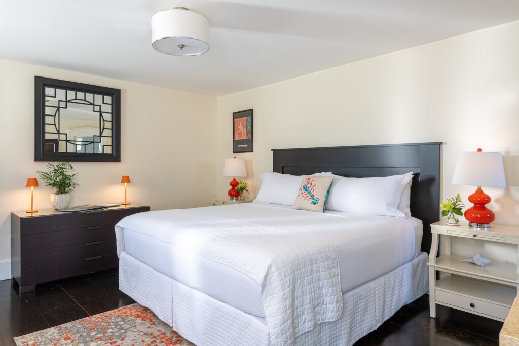 A white bed with a red lamp on a nightstand beside it at a beautiful Cape Cod Bed and Breakfast.